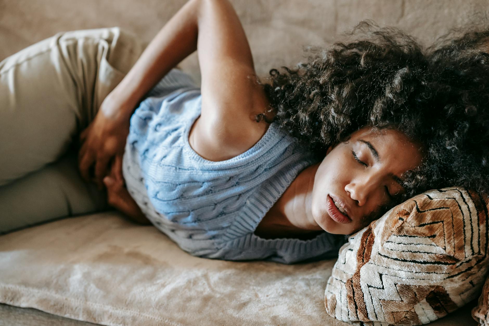 Persistent Bloating and Abdominal Discomfort - Liver Health Symptoms Woman lying on sofa experiencing abdominal pain and bloating, a common sign of poor liver health
