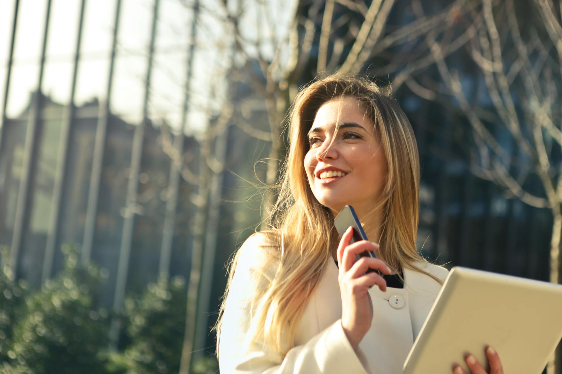 Confident businesswoman smiling outdoors while holding her phone and tablet, representing how smile confidence psychology plays out in daily professional life