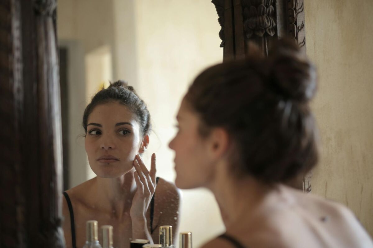 Woman Skincare Routine Examining Face in Mirror Woman examining her skin in a mirror during a skincare routine