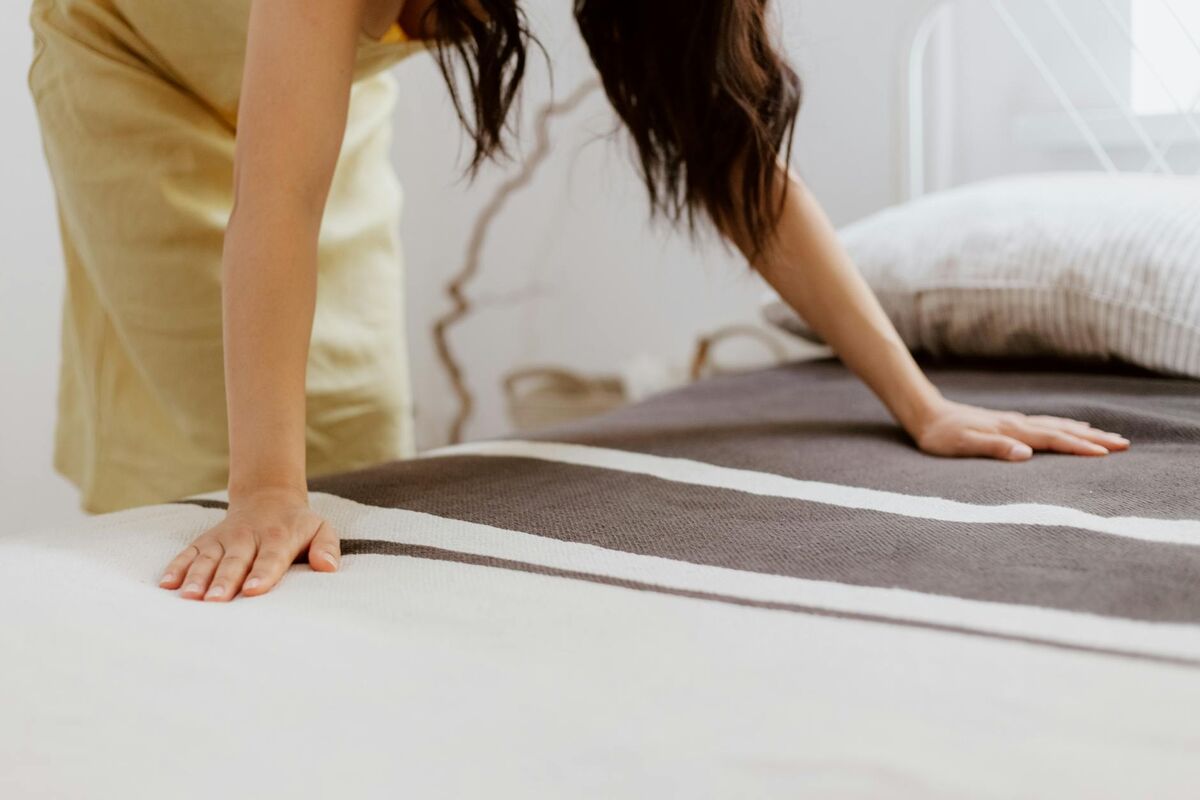 Proper sheet tucking technique for keeping fitted sheets on the bed Woman making a bed and tucking in striped sheets in a bright bedroom