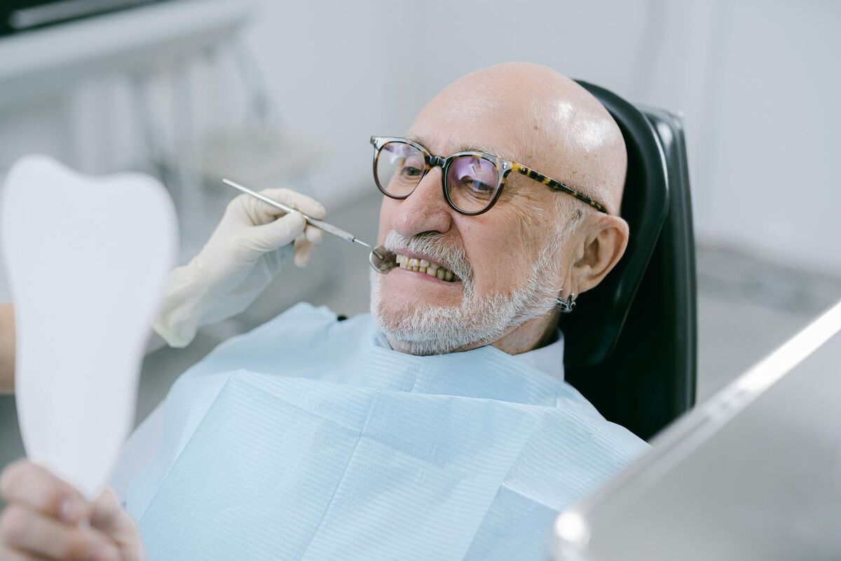 Elderly man examining his teeth with a dental mirror during a checkup